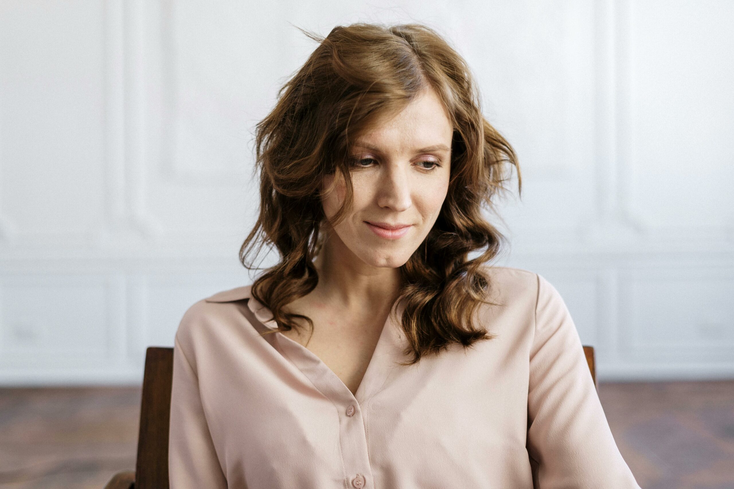 A woman with curly hair sitting thoughtfully in an indoor setting, conveying peace and contemplation.